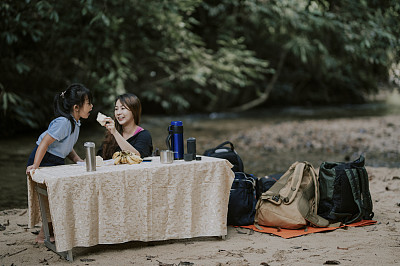 一位亚洲华人母亲在丛林的河边给她的女儿吃面包早餐