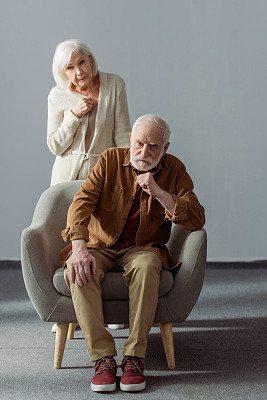 沮丧的老年妇女触摸胸部，而站在丈夫身后，生病的痴呆症