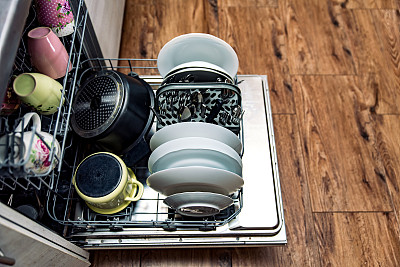 打开洗碗机，在篮子里放干净的盘子，杯子和不锈钢餐具。厨房洗碗机在厨房