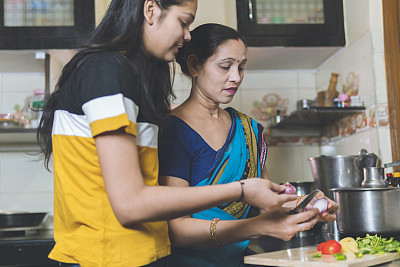 印度妈妈教女儿切菜，女儿在厨房帮妈妈做饭。