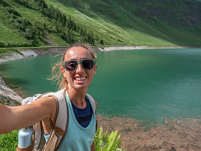 年轻女子在美丽的高山湖周围徒步旅行时自拍