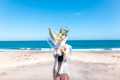 年轻女子在海滩上用花束遮住脸