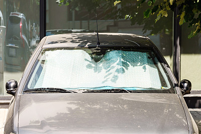 在户外停了一天的灰色汽车挡风玻璃下的遮阳板可以保护它不被太阳晒伤。金属银箔制成的箔式遮阳板可以直接反射阳光。