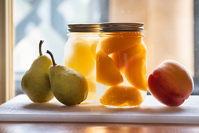 新鲜罐头梨和桃子在阳光明媚的厨房柜台