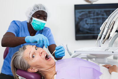 成年女性病人坐在牙科椅上。牙医正在治疗一位女病人