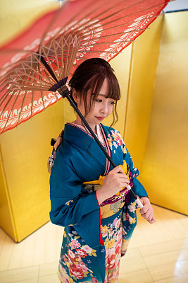 在“Seijin Shiki”成年仪式上，身着furisode和服的年轻女子手持纸伞，站在金色的“Byobu”折叠屏风前