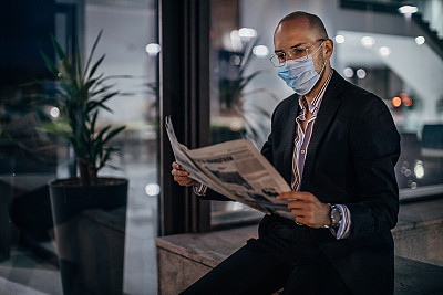 一位戴着防护面罩的商人坐在喷泉边看报纸