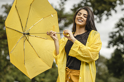 快乐幸福的女人穿着黄色的雨衣，拿着黄色的雨伞，在雨天享受