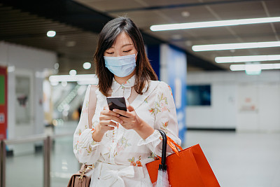 一名亚裔华人女子戴着口罩在地铁站打电话