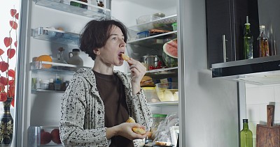 成熟的女人在冰箱旁边吃橘子