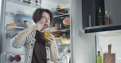 成熟的女人在冰箱旁边吃蜂蜜
