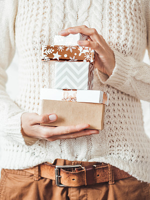 女士缆线编织白色毛衣与斯堪的纳维亚图案和棕色斜纹裤与皮带。手里拿着一堆圣诞礼物。新年庆祝休闲装。