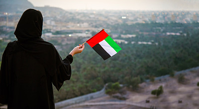 日落时分，一名阿联酋妇女在沙漠山区举着阿联酋国旗