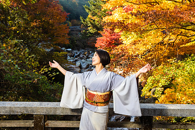 在小野的日本老年女子与秋天的枫叶跳舞