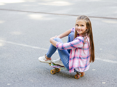 可爱的小女孩坐在滑板和思考。十几岁的孩子在户外吃便宜货