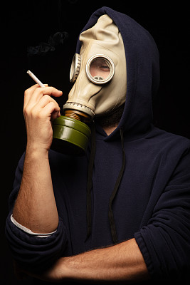 年轻男子的肖像在防毒面具手里拿着香烟。