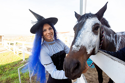 为了庆祝万圣节，一个打扮成女巫的女孩展示了一张涂着白漆的马脸