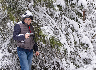 这个人感到冷了，就用热咖啡暖暖身子。一个中年白人男子走在冬天的森林里。步行旅游。