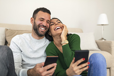 微笑的男人和女人一起看手机屏幕，年轻的夫妇一起看有趣的视频，在社交网络上聊天，在信息中阅读好消息，玩游戏，网上购物