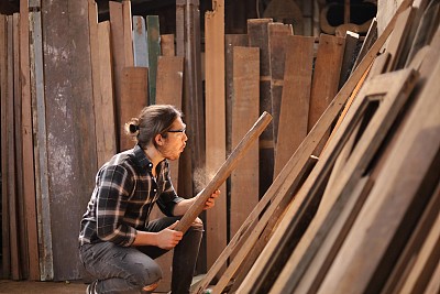年轻的白种木匠正在他自己的车库风格的车间里，为了爱好，从木板上吹锯末