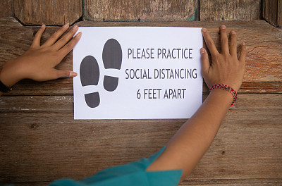 在木墙上挂着“请保持社会距离”标志的陌生女人