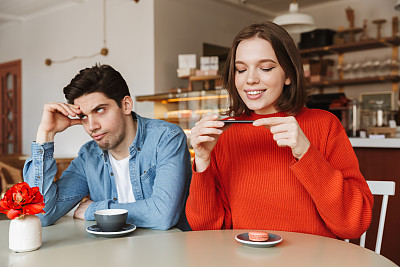 一个白种人无聊的照片，而他的女朋友正在咖啡馆里拍马卡龙饼干