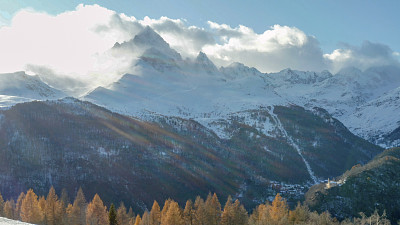 雪山与云彩和秋天的树木前景