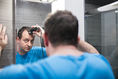 一名身穿t恤的男子在浴室的镜子前用理发器给自己理发，在隔离冠状病毒大流行的冠状病毒19，呆在家里的概念