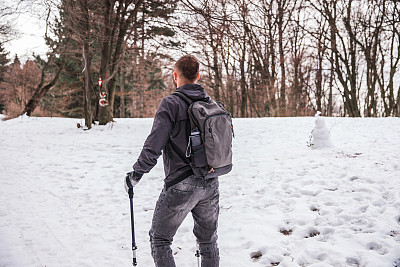 后视图的一个徒步旅行者穿着背包和行走在雪地上与徒步杆子