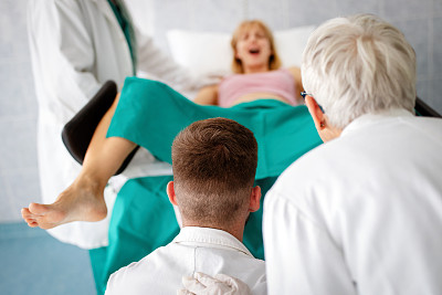 在医院里，待产妇女推着分娩，产科医生在一旁协助