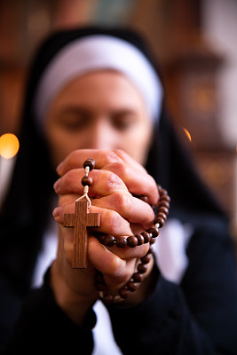 修女在教堂祈祷，双手紧握念珠。