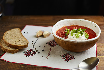 木桌上手工陶碗里的罗宋汤配酸奶油。包括面包，青葱，辣椒和大蒜。传统的乌克兰菜。
