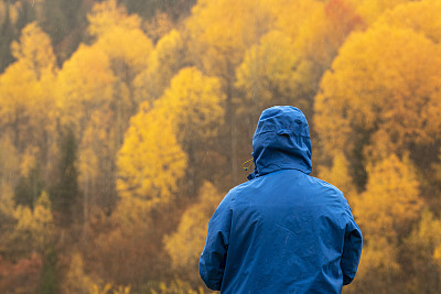 在秋天，一个穿着蓝色雨衣、看向别处的不可辨认的男人。