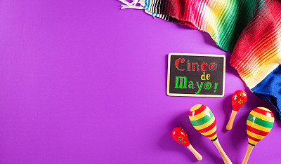 Cinco de Mayo假日背景由沙球，墨西哥毛毯条纹或雨披serape在紫色背景与文字。