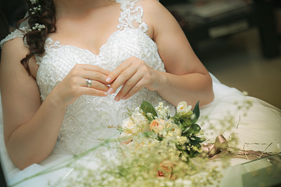 新娘穿着漂亮的礼服，膝盖上放着婚礼花束