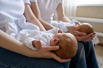 刚出生的同卵双胞胎在床上，在父母的手上。生活方式，孩子的情感。婴儿婴儿与复制空间