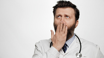 医生打了个哈欠。疲倦无聊的男人医生在白色的背景打呵欠，用手捂住他的嘴