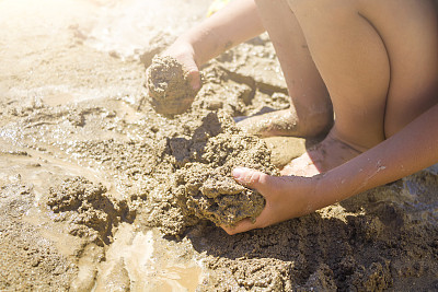 光着脚玩湿沙的孩子。小男孩在夏日阳光明媚的日子里揉捏捏泥。