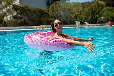 在一个炎热的夏天，一个美丽的女孩在充气甜甜圈上的游泳池里玩得很开心