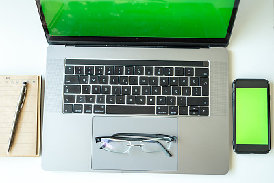 家庭办公室设置笔记本电脑与绿屏智能手机与绿屏笔记本和笔都在白色桌子上横微距拍照