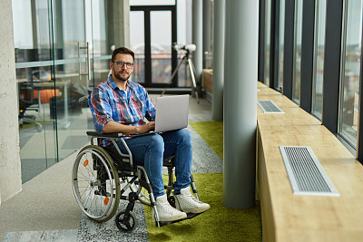 残疾人男性IT工作者在轮椅上使用笔记本电脑工作