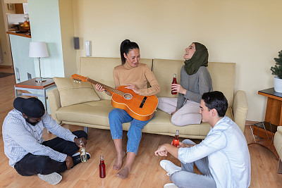 一群不同种族的朋友在家里弹吉他喝啤酒。