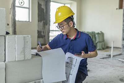 亚洲男性工程师，在装修工地处理建筑图纸和手机