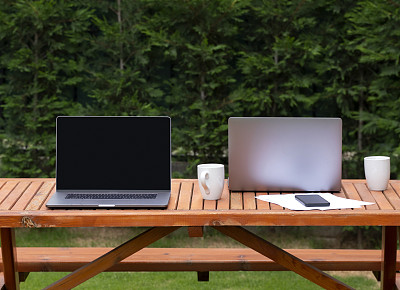两台现代笔记本电脑放在后院的木桌上，在家工作的概念