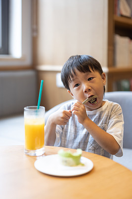 这个小男孩正在喝果汁，吃甜点