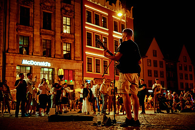 街头音乐表演。男人拿着吉他在夜晚的城市街道上唱着歌。波兰弗罗茨瓦夫——2021年8月14日