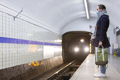 戴着防护口罩的男子在地铁站等车。COVID-19爆发，冠状病毒流行