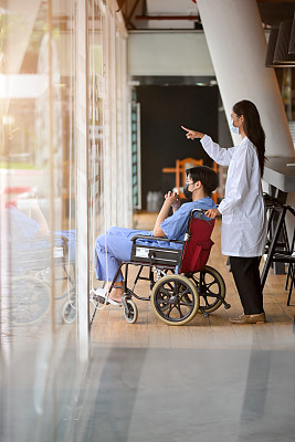 在一名医生的陪同下，坐着轮椅的男病人坐在医院的走廊里。