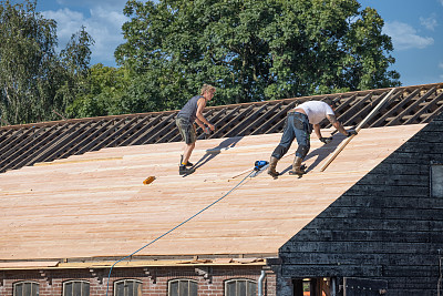 两个建筑工人正忙着修理木棚的屋顶