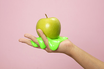 手握切片的绿色苹果在绿色的纸背景。
